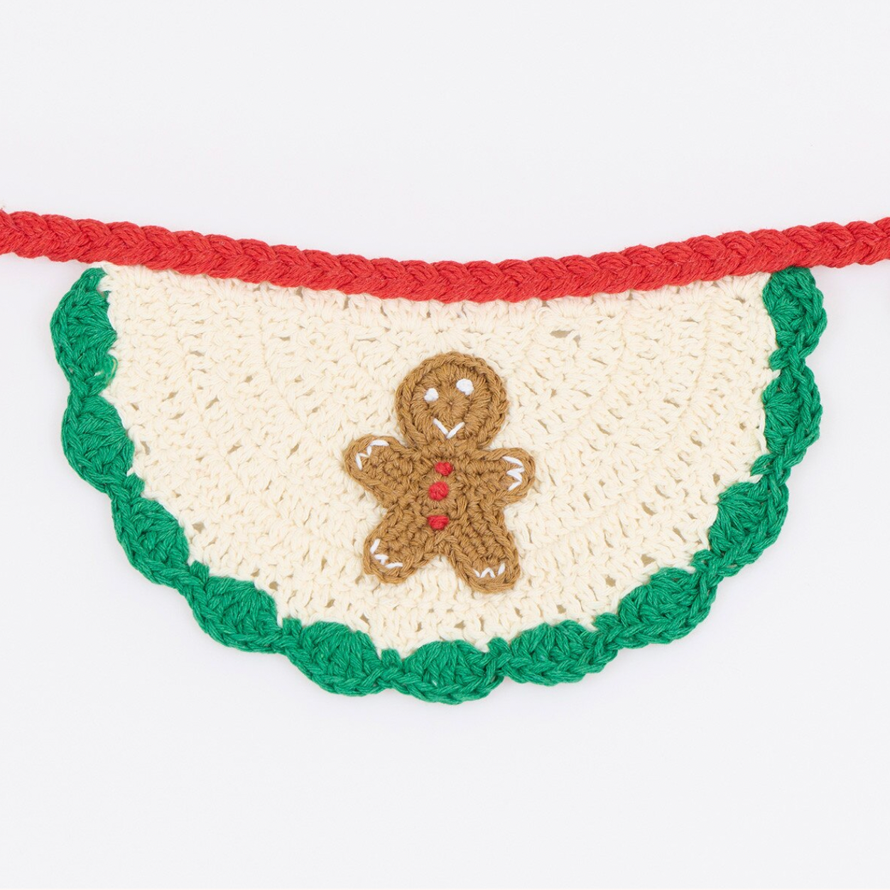 A crocheted holiday bunting garland featuring a scalloped green edge, a red top border, and a central beige gingerbread man figure with red buttons on a cream background.