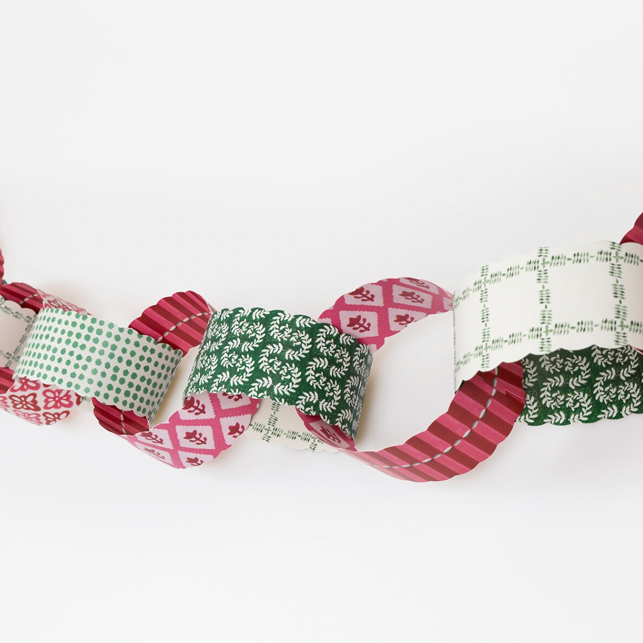 A festive washi tape garland made of overlapping loops in holiday patterns, including green with white snowflakes, red with white snowflakes, green with white dots, and green with white plaid, shown against a plain white background.
