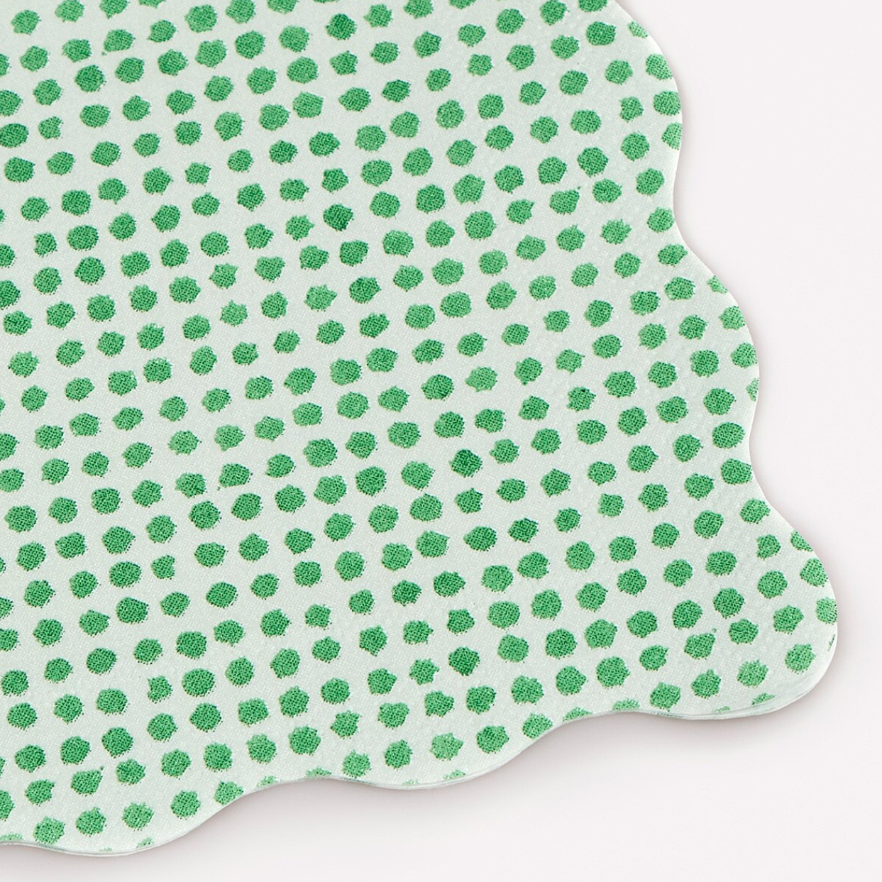 A scalloped-edge paper napkin with a white background and a pattern of small green hand-drawn polka dots, shown on a light gray background.