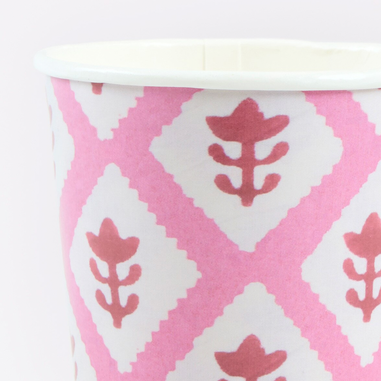 A close-up of a paper cup featuring a pink and white geometric ikat pattern with stylized leaf motifs.