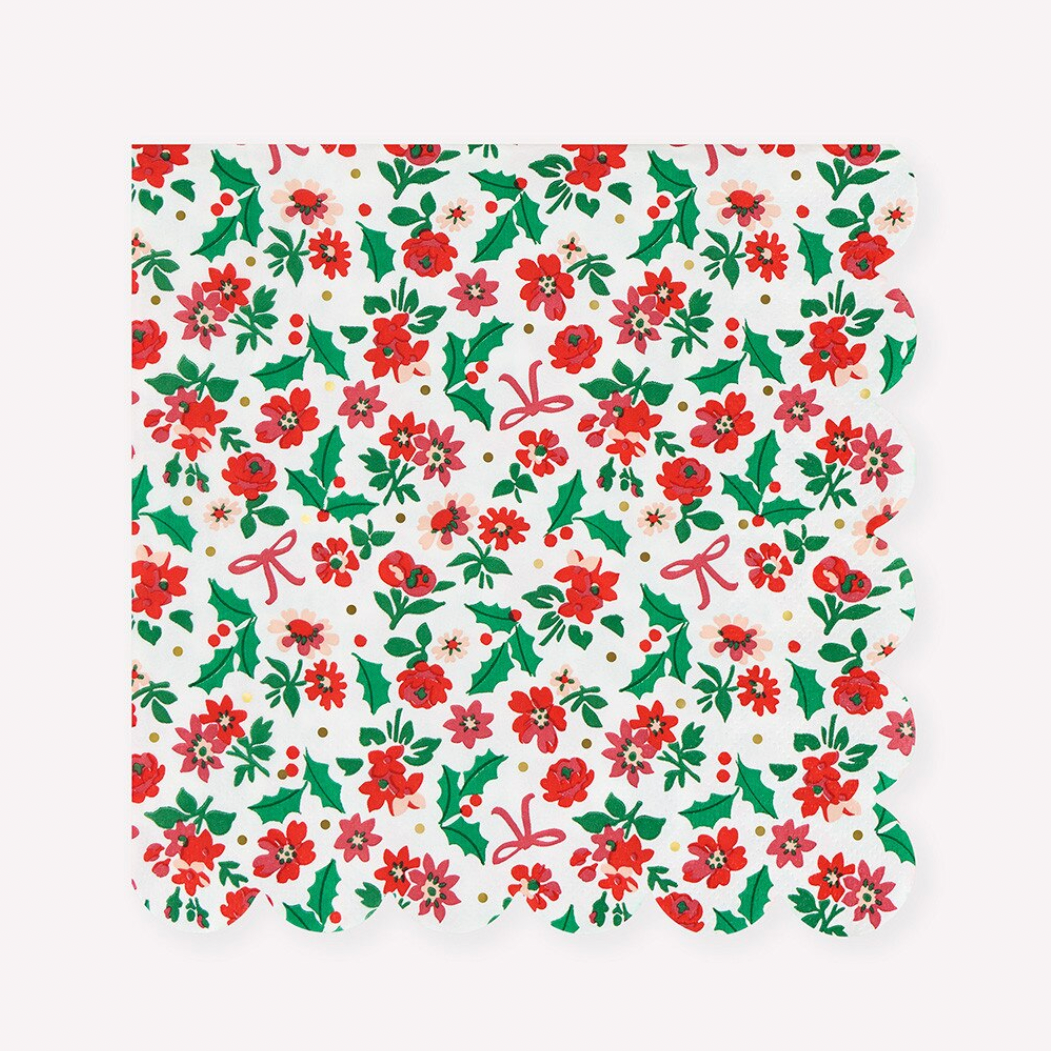 A square paper napkin with a scalloped edge, featuring a festive Christmas pattern of red poinsettias, green holly leaves, and pink bows on a white background.