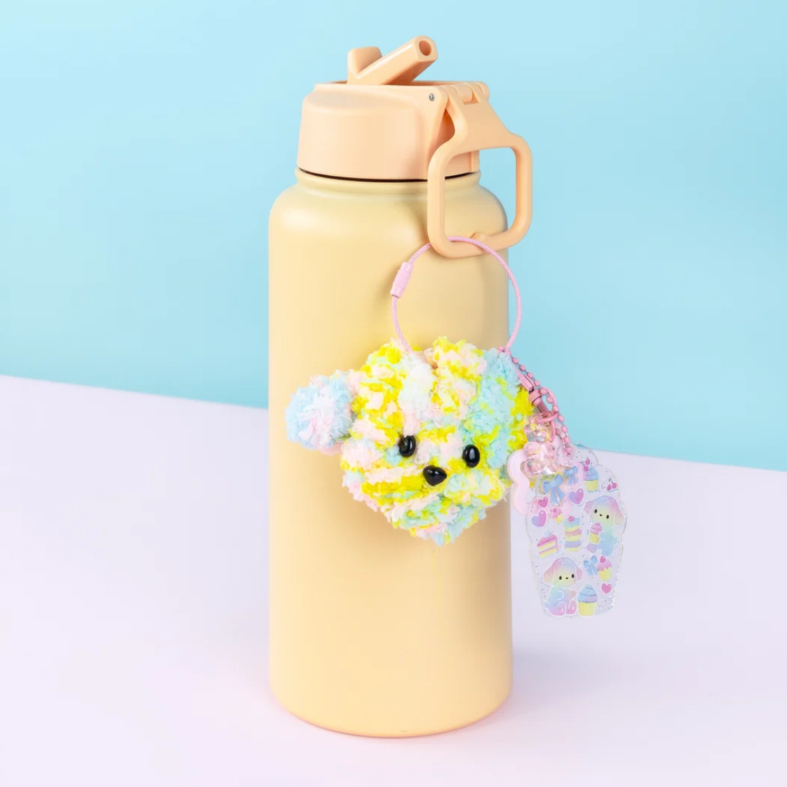 Yellow water bottle with a pink lid and floral charm on a light blue background