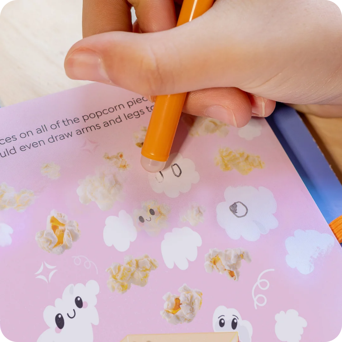 Hand holding a pen over a pink book with cartoon popcorn illustrations