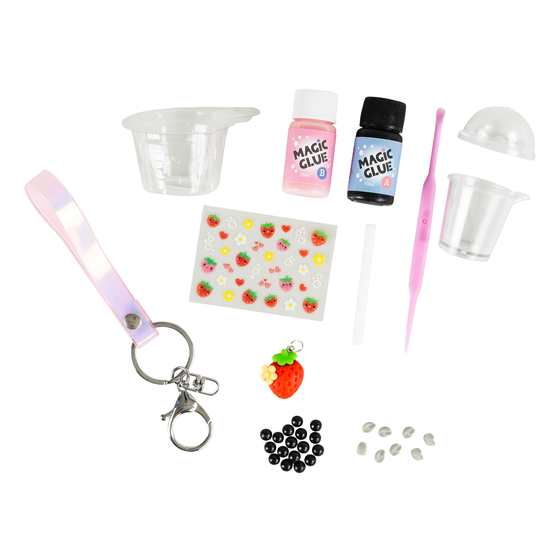 A DIY resin craft kit with various small tools and components, including a pink LED keychain, miniature bottles of 'Magic Glue', a strawberry-shaped charm, beads, and plastic cups, all arranged on a white background.