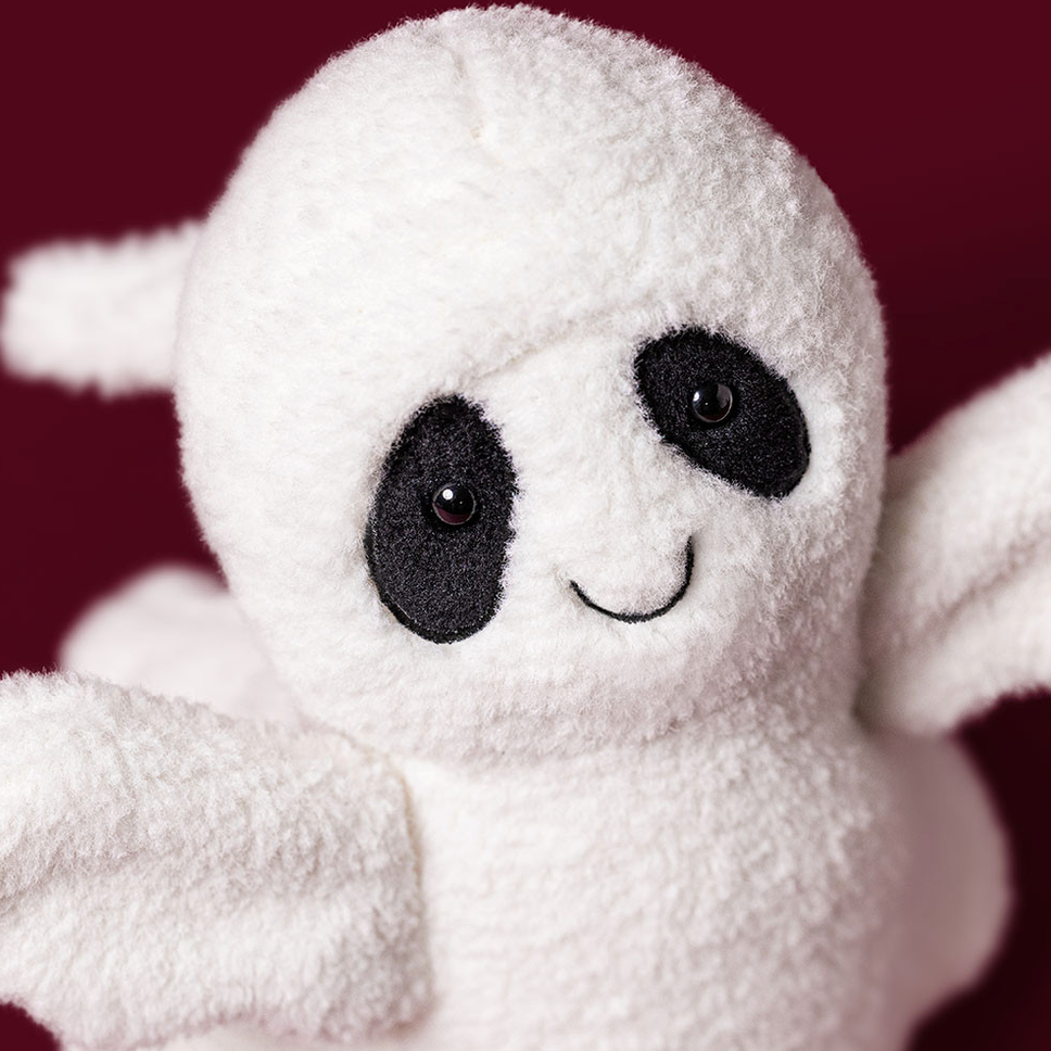 A plush ghost toy with a white fuzzy body, black embroidered eyes, and a stitched smile on a dark burgundy background. 