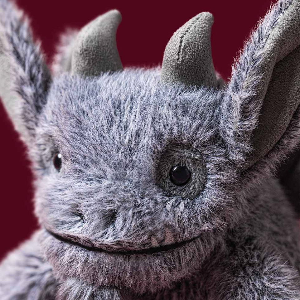 A close-up of a gray plush toy with large pointed ears, small horns, and a stitched smile against a dark red background.