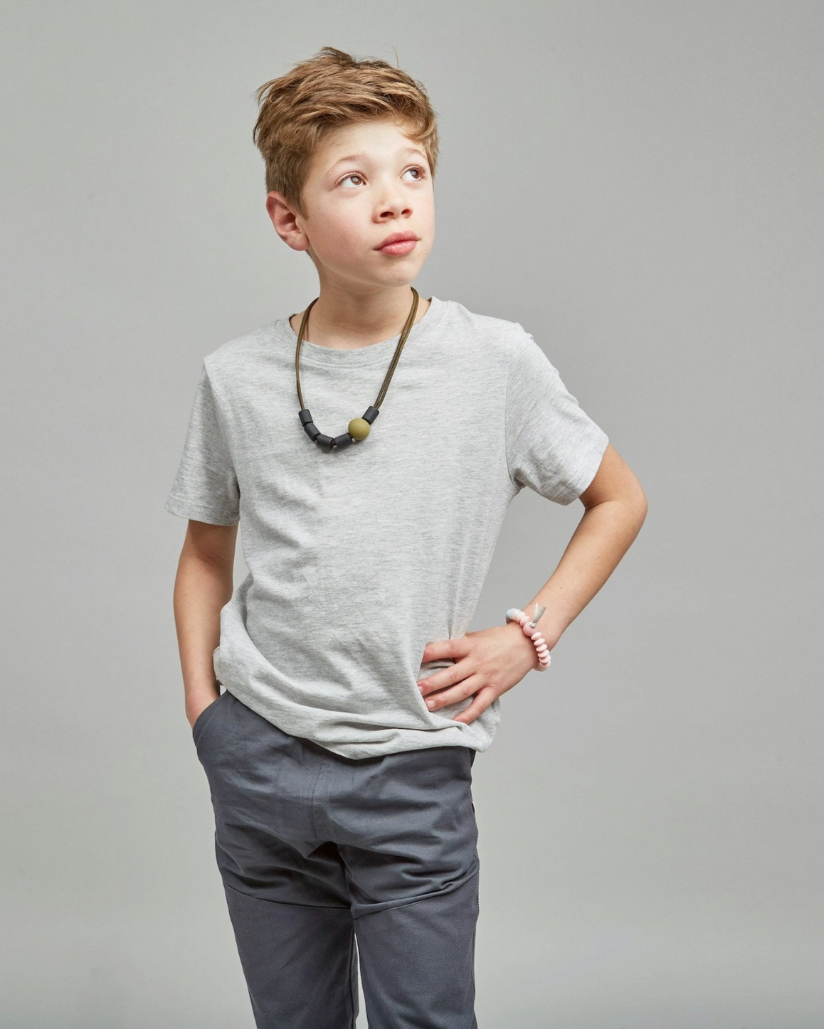 Young boy wearing a gray t-shirt and dark pants against a plain background