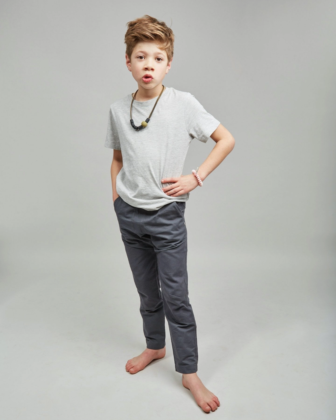 Young boy wearing a white t-shirt and gray pants on a plain background