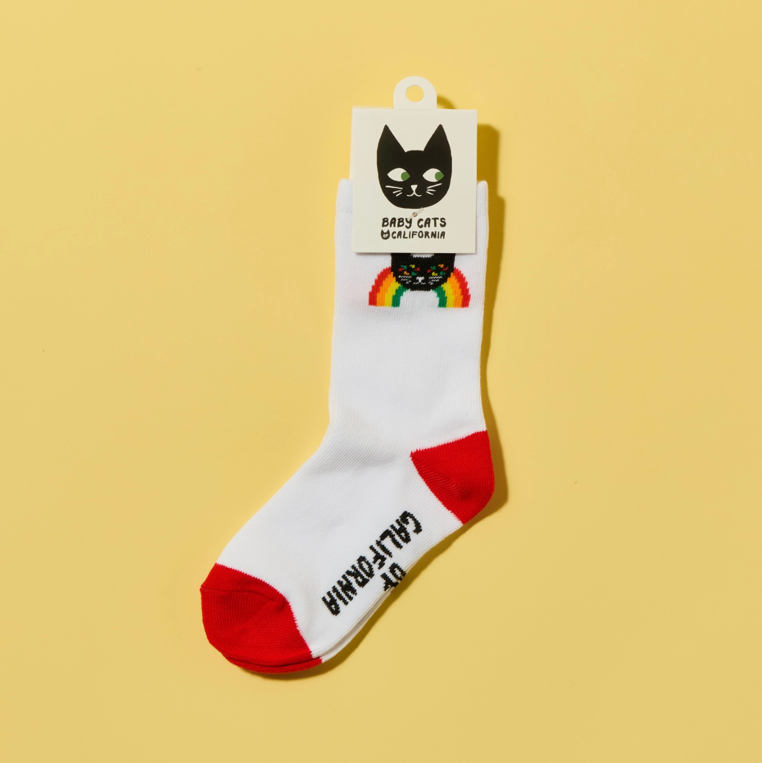 White sock with red toes and soles, featuring a rainbow and cat design, on a yellow background.