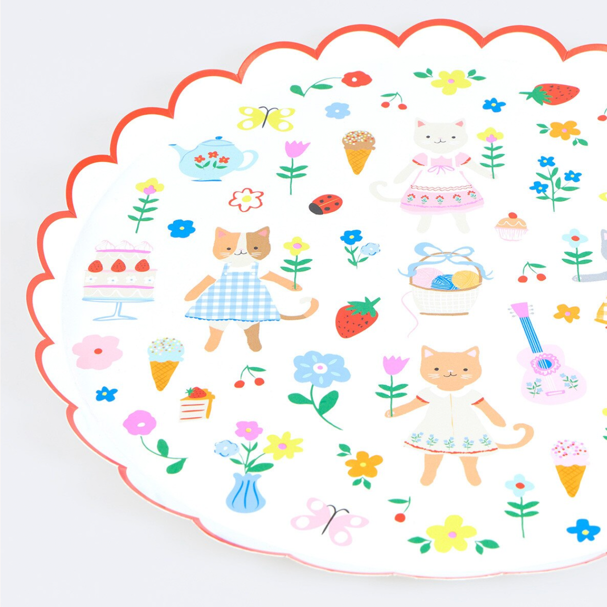 A scalloped white plate with a red border, decorated with cute pastel illustrations of cats, flowers, strawberries, cakes, butterflies, and small whimsical objects on a light background.