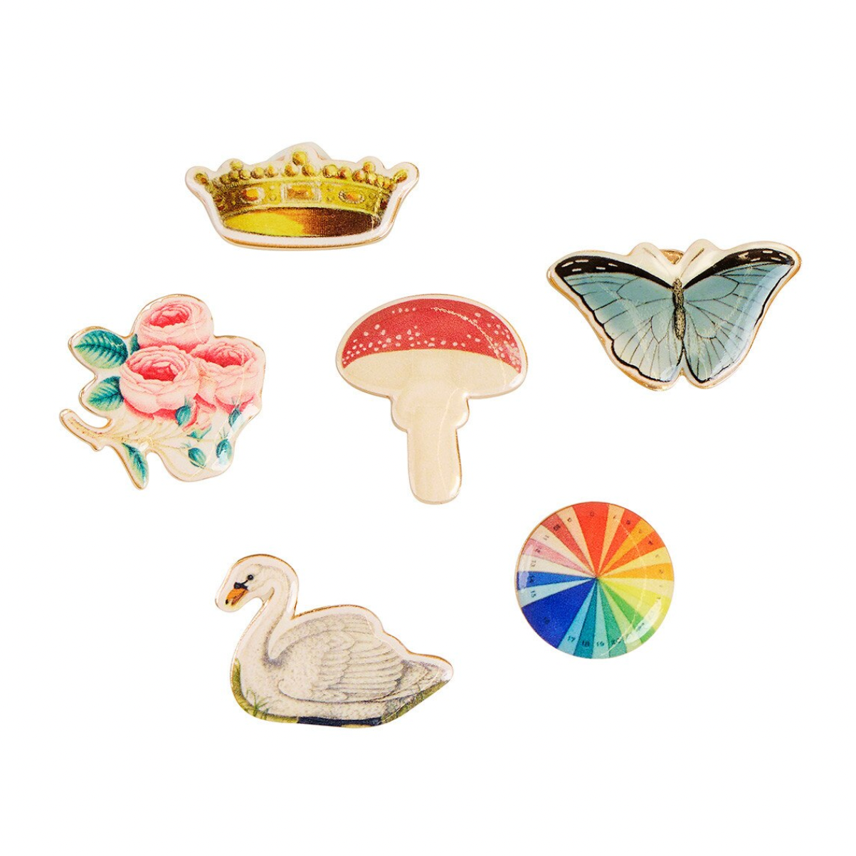 Six decorative enamel pins arranged on a white background, including a gold crown, pink roses, a red-and-white mushroom, a blue butterfly, a white swan, and a circular rainbow design.