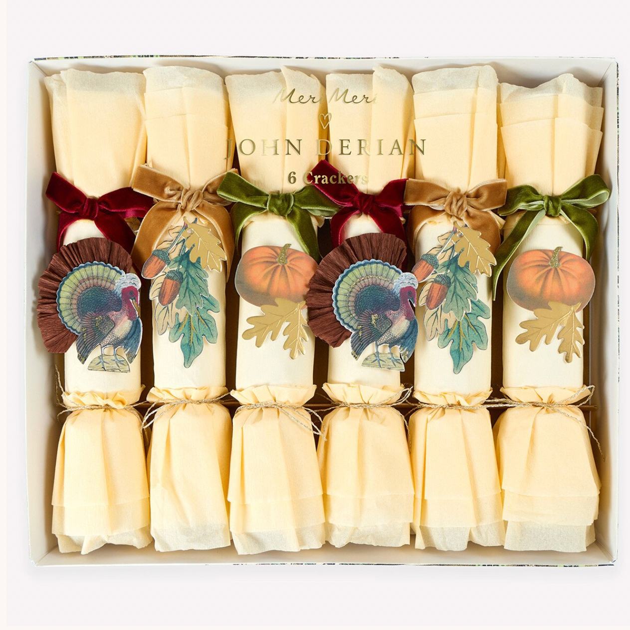 A boxed set of six John Derian Christmas crackers arranged in a white gift box. Each cracker is wrapped in cream paper with autumn-themed illustrations including pumpkins, leaves, and a turkey, and tied with red or green ribbon bows.