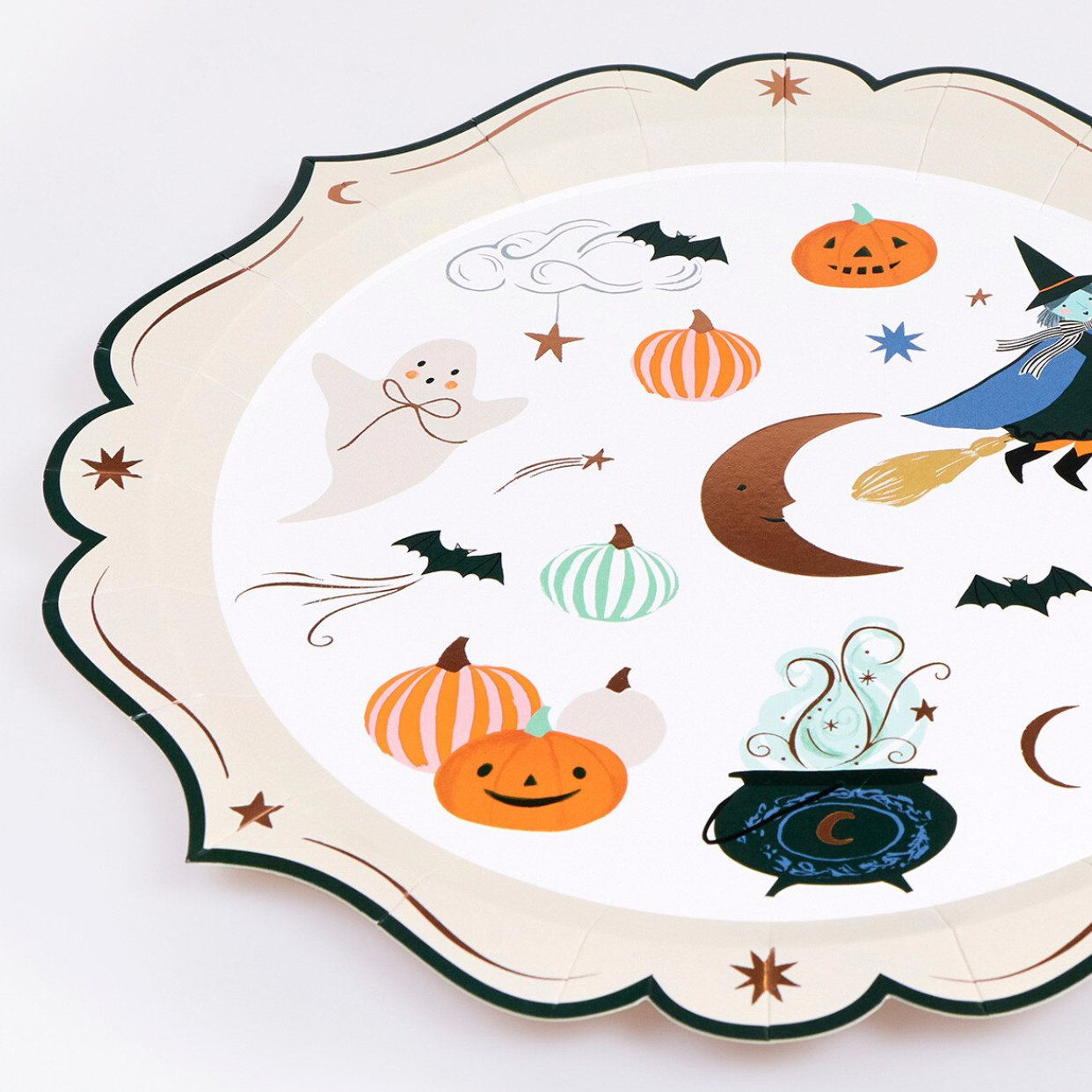 A scalloped paper plate with a white background and a colorful Halloween print, featuring pumpkins, a ghost, a witch on a broomstick, bats, a crescent moon, stars, and a cauldron.