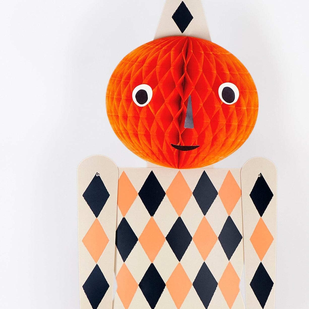 A Halloween-themed decorative paper cutout figure with a round orange jack-o'-lantern head, black nose, white eyes, and a patterned body in cream, orange, and black diamonds, shown against a plain white background.