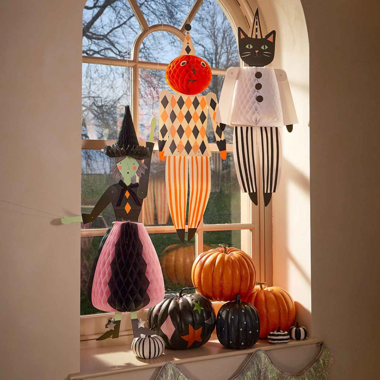 Halloween-themed hanging decorations displayed on a windowsill with pumpkins. The set includes a witch figure with a pink honeycomb skirt, a cat figure in a white tuxedo, a striped pumpkin, and other small seasonal ornaments.