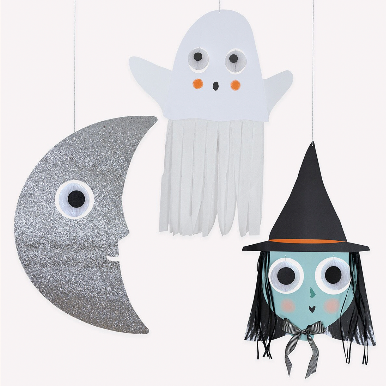 Three handmade Halloween hanging decorations on a plain white background: a silver glitter crescent moon with a large googly eye, a white ghost with orange cheek accents, and a witch figure with a black hat, black fringe hair, and a gray ribbon bow.