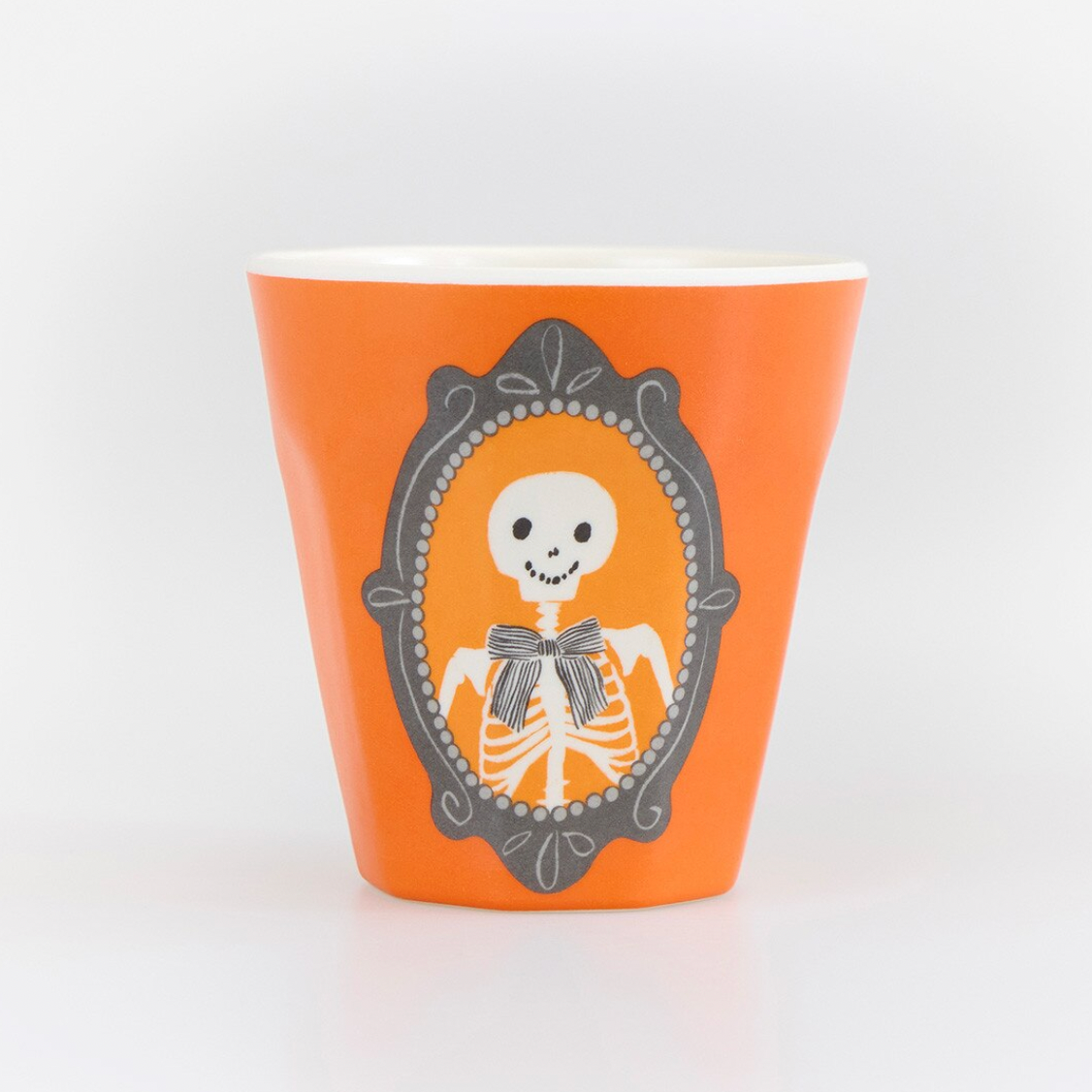 An orange ceramic cup featuring a Day of the Dead style skeleton graphic in a gray ornate frame, set against a clean white background.