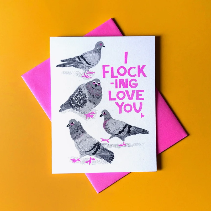 A white greeting card with watercolor-style pigeon illustrations and pink text reading 'I FLOCKING LOVE YOU' is displayed on top of a bright pink envelope against a warm yellow-orange background.