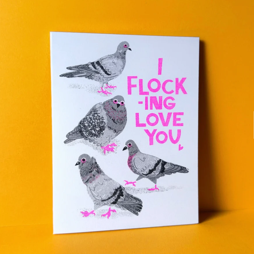 A white greeting card featuring illustrations of four pigeons in gray and black, with bright pink text reading 'I FLOCKING LOVE YOU' and pink accents, displayed against a solid orange-yellow background.