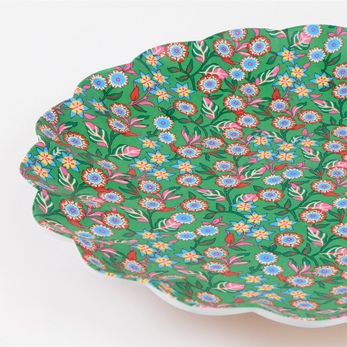 A close-up of a scalloped plate with a vibrant green background and a dense, colorful floral pattern featuring blue, pink, yellow, and white flowers with red and green leaves.