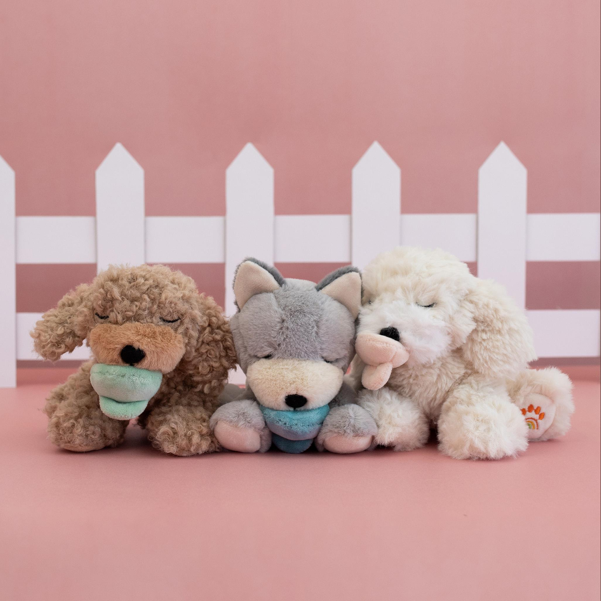 Three plush toys, including a dog, wolf, and cat, sitting together against a pink background with a white picket fence.