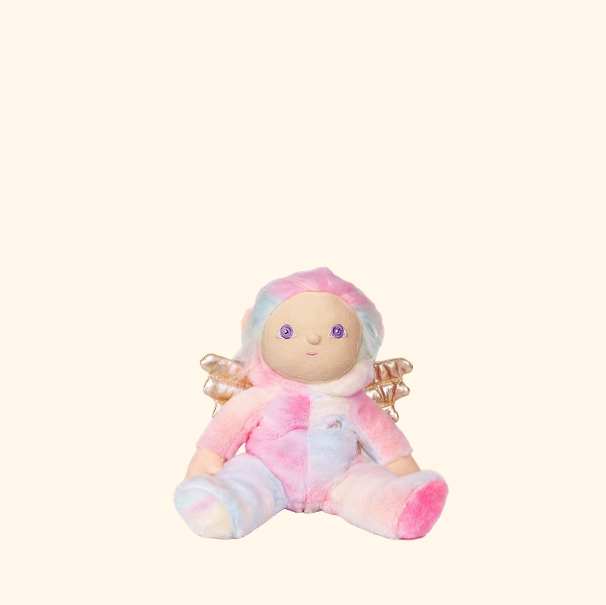 A small plush doll with pastel pink, blue, and lavender tie-dye coloring, featuring a round face, purple eyes, tiny gold wings, and seated pose on a solid cream background.