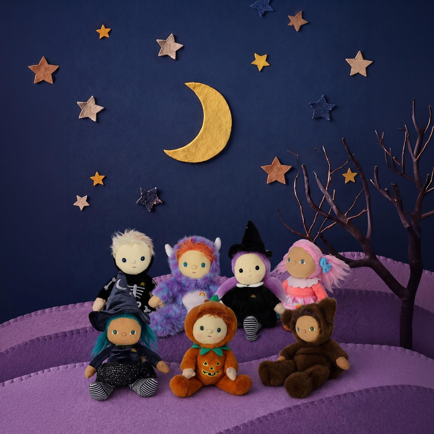 Six plush dolls dressed in Halloween costumes are arranged on a purple felt landscape with a dark blue sky backdrop, decorated with felt stars, a gold crescent moon, and a bare tree branch.