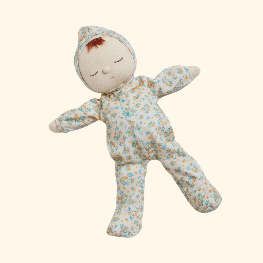 A plush baby doll wearing a light cream floral onesie with blue and yellow flowers, set against a solid pale beige background.