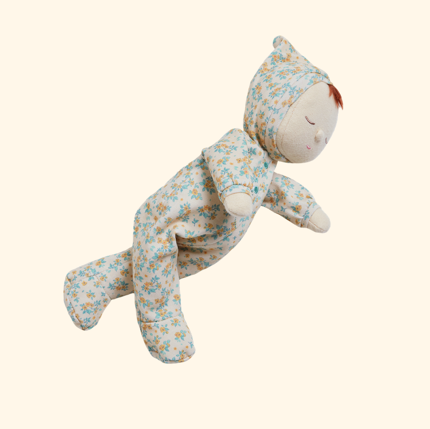 A plush doll dressed in a one-piece floral pajama set, floating against a solid cream background.