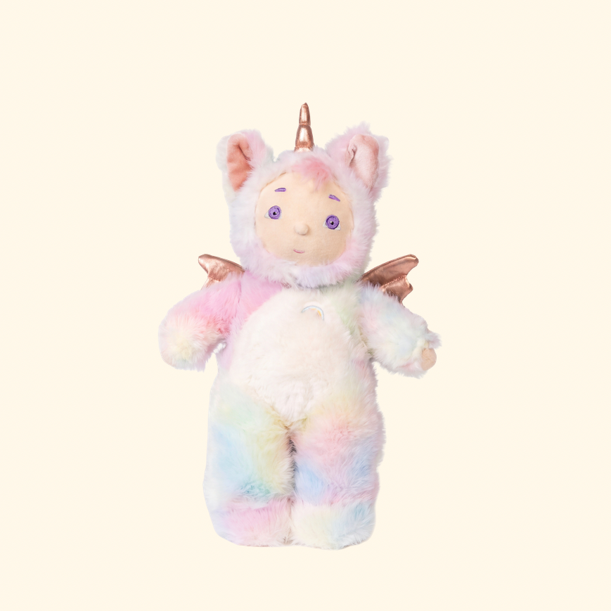 A pastel rainbow plush unicorn toy with a horn, wings, and cat ears, centered on a plain cream background.