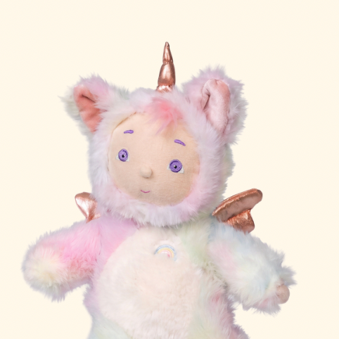 A plush unicorn doll with pastel rainbow-colored fur, featuring a horn on its head, small wings, and a soft embroidered face, shown against a solid cream background.