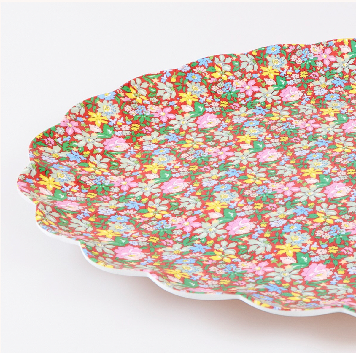A close-up of a scalloped ceramic plate with a dense, colorful floral pattern on a white background.