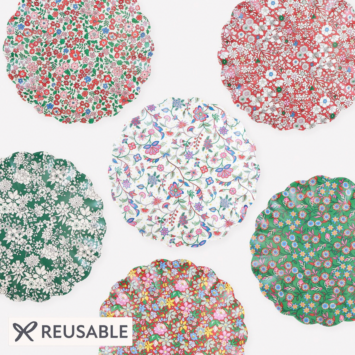 Six reusable scalloped fabric placemats with various colorful floral prints are arranged on a white background. An 'REUSABLE' label with a scissors icon is in the bottom-left corner.