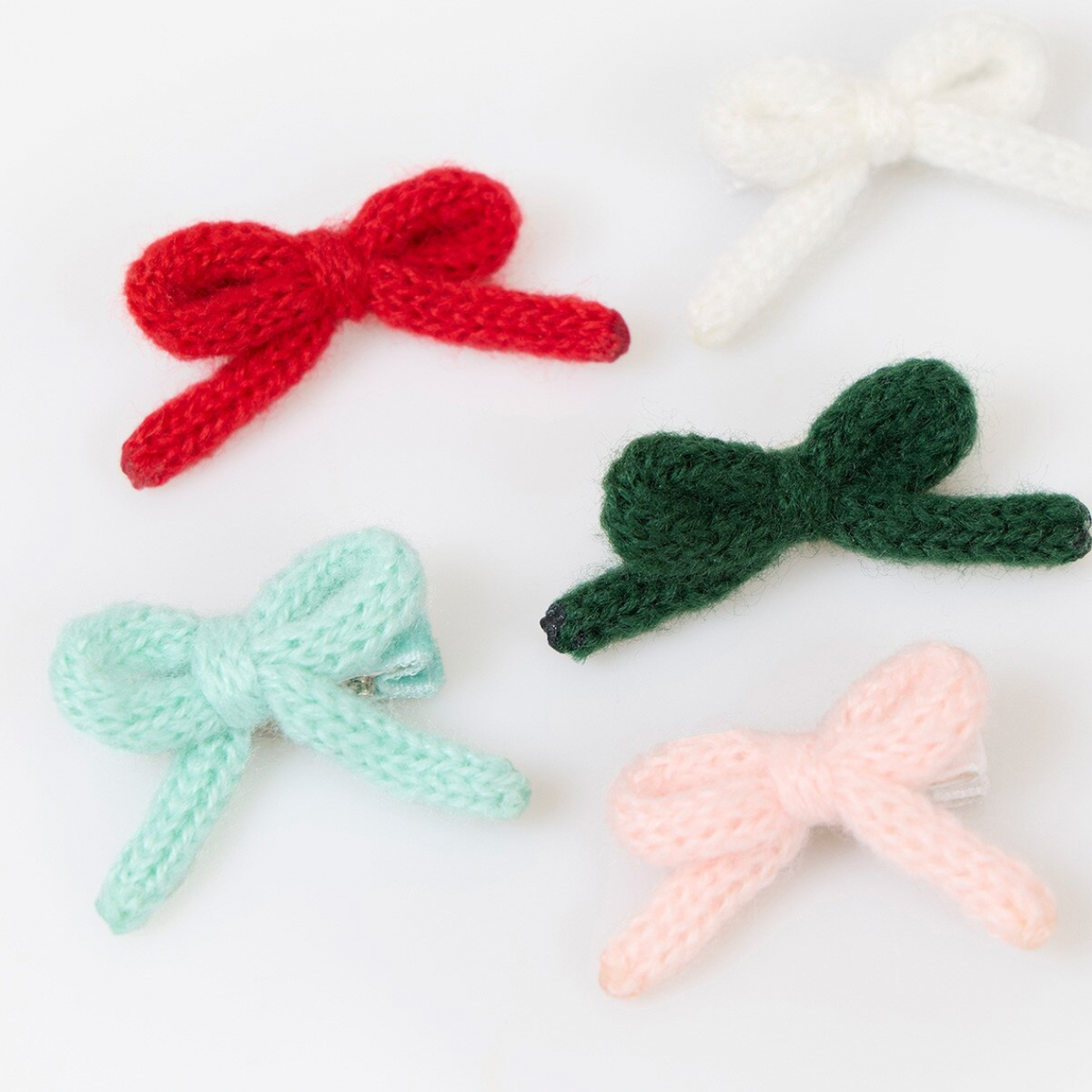 Four knitted bow hair clips in red, white, mint green, and light pink, arranged on a clean white background.