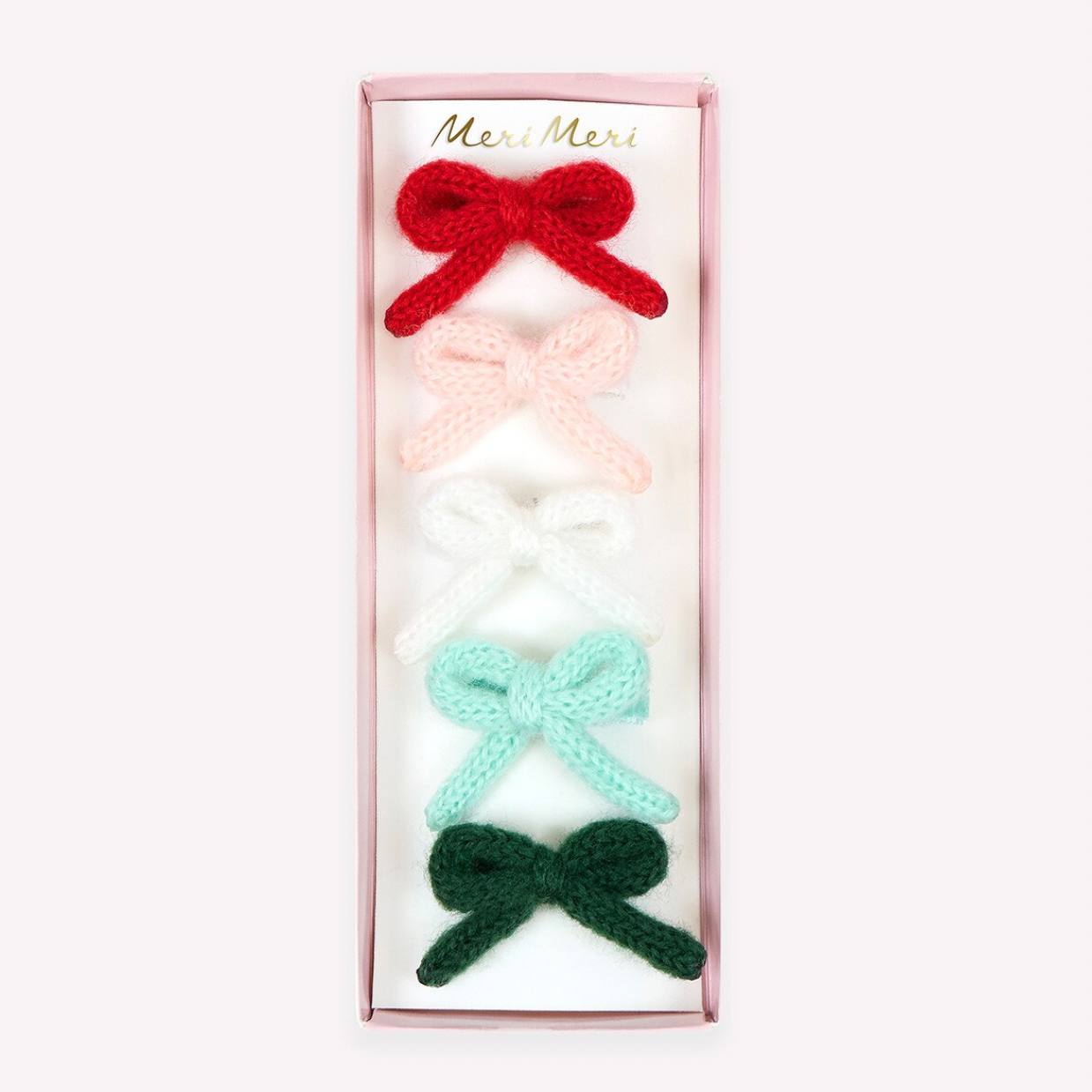A set of five knitted bow hair clips in red, light pink, white, mint green, and dark green, presented in a vertical pink box with the brand name 'Meri Meri' printed at the top.