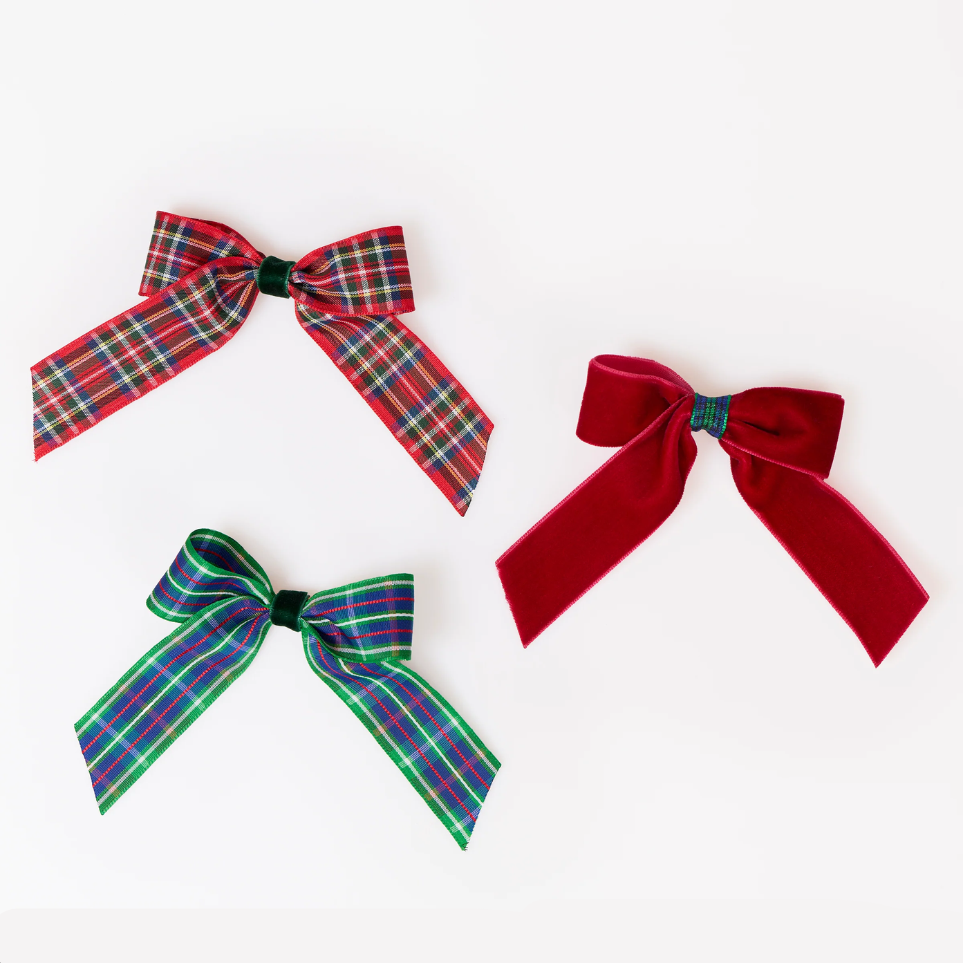 Three ribbon hair bows arranged on a plain white background: two plaid bows in red/green tartan and one solid red bow.
