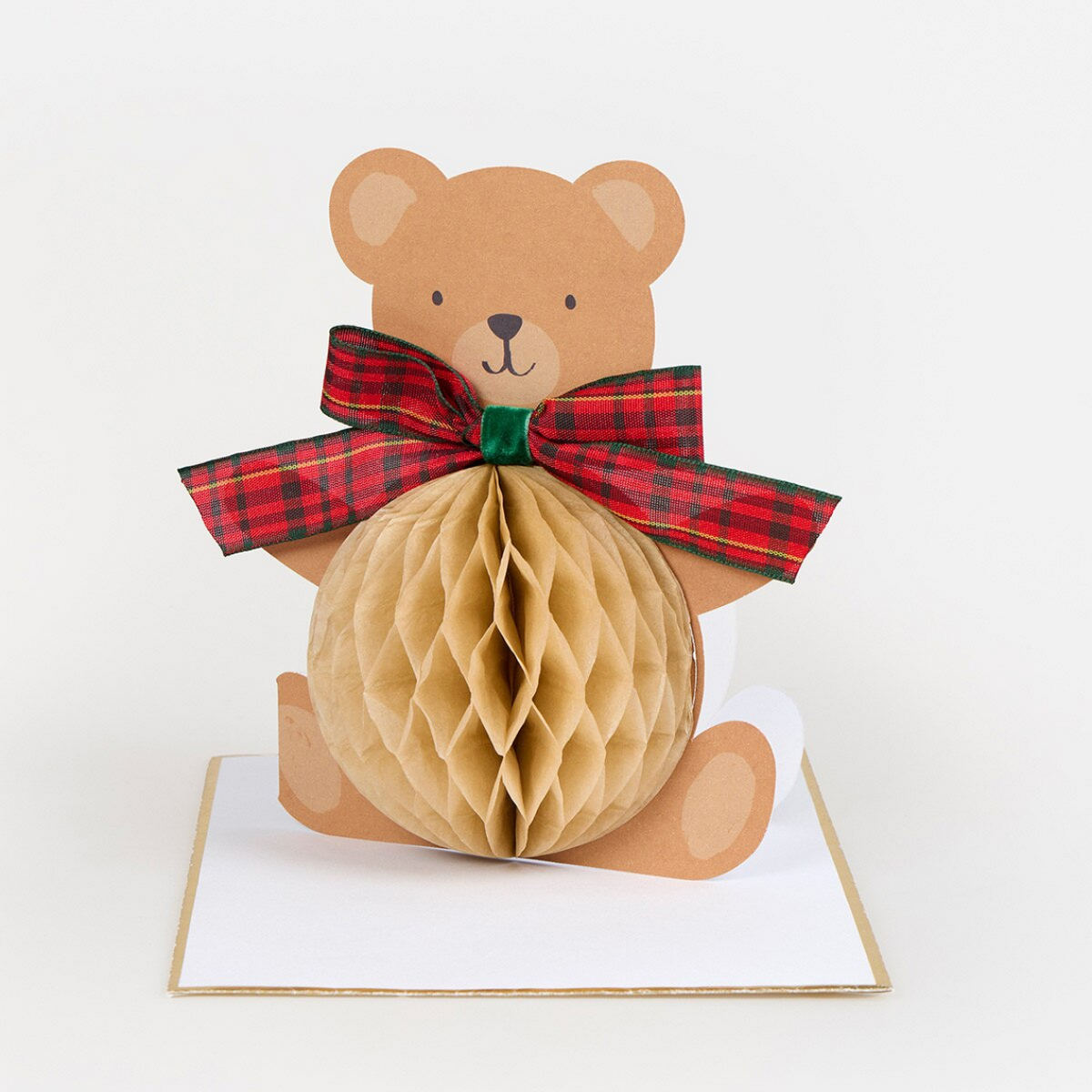 A 3D papercraft pop-up card featuring a brown teddy bear holding a honeycomb ball, decorated with a red and green plaid ribbon bow, sitting on a white card base.