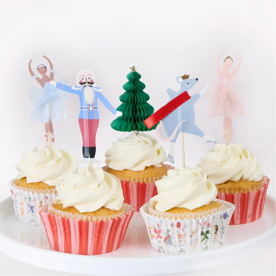 Cupcakes with white frosting and red paper liners, topped with festive cake toppers on a white background.