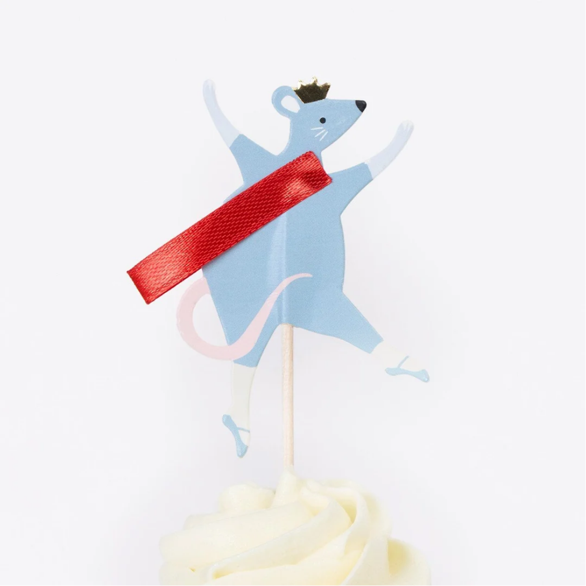 A light blue mouse party topper with a red sash and small crown, mounted on a wooden stick and placed in the center of a white frosted cupcake against a plain white background.