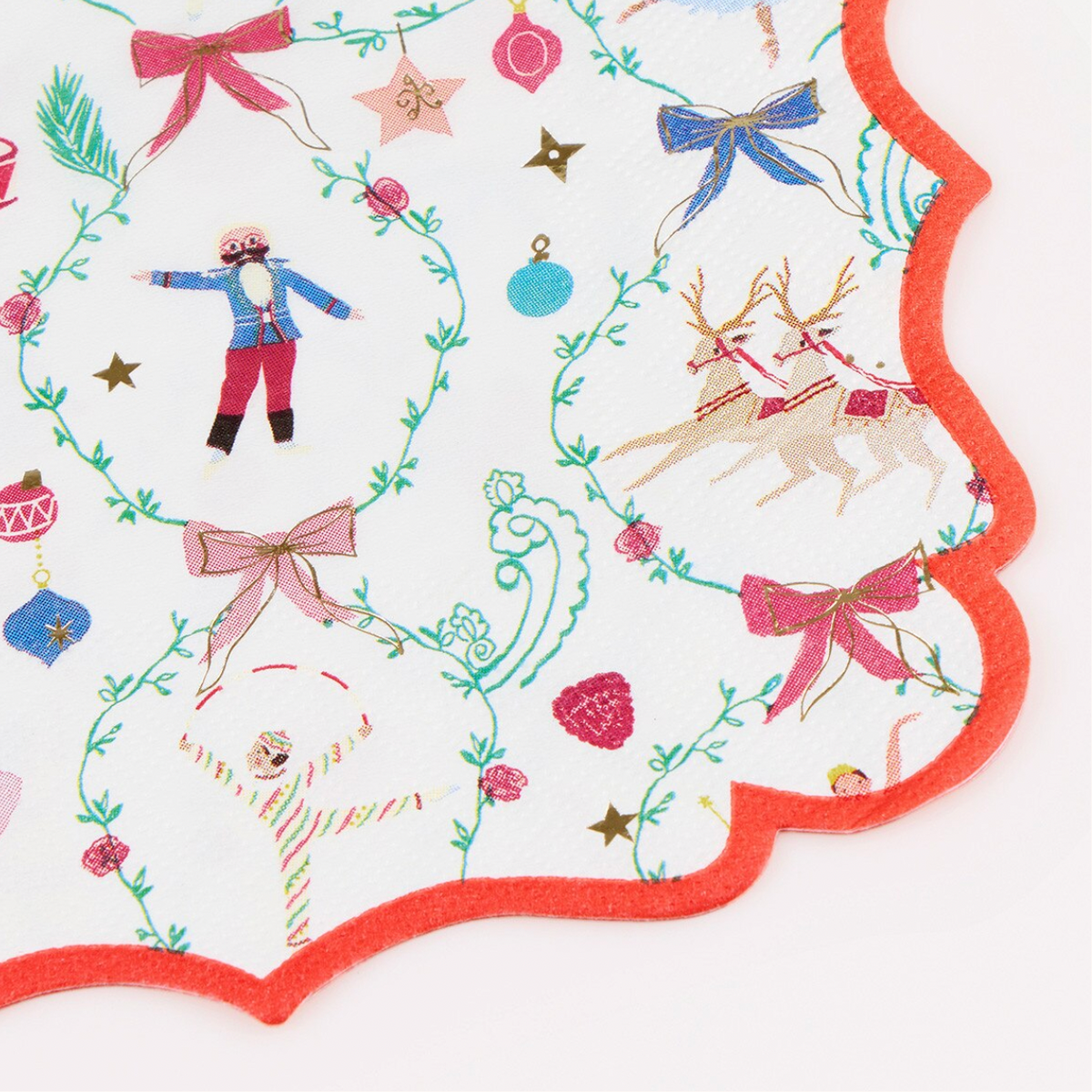 A close-up of a scalloped white fabric napkin or paper with embroidered Christmas motifs, including bows, stars, ornaments, a reindeer, and a small figure, finished with a red-orange border.