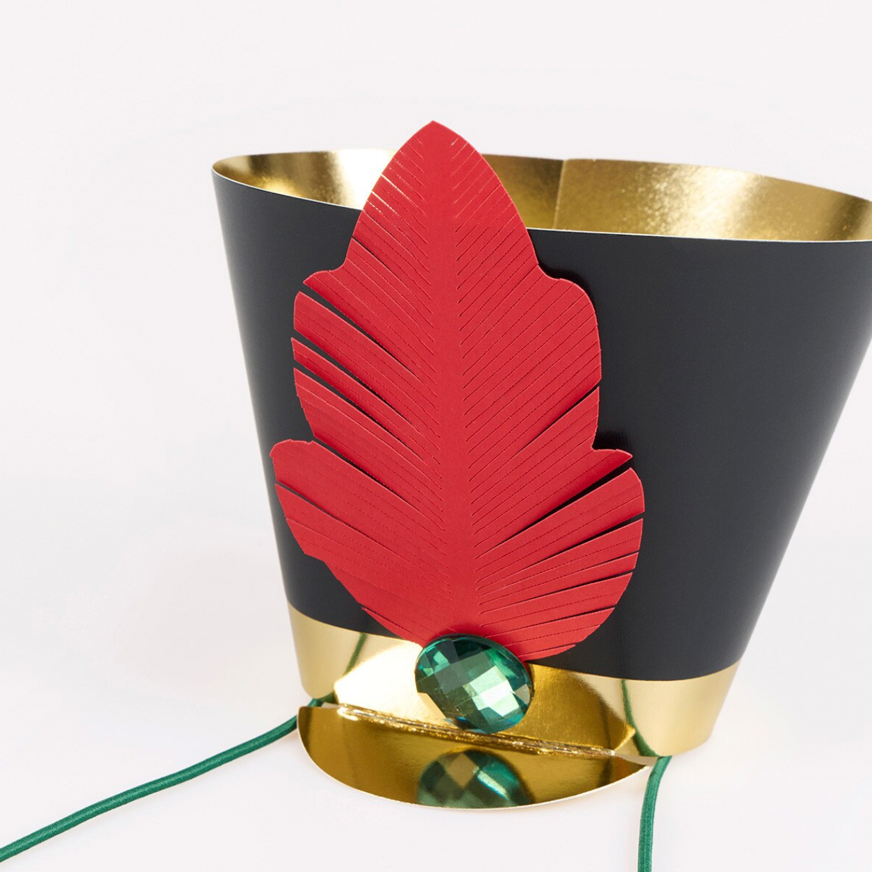 A black and gold metallic cone-shaped hat with a large red leaf applique and a faceted green gemstone, shown on a white background.