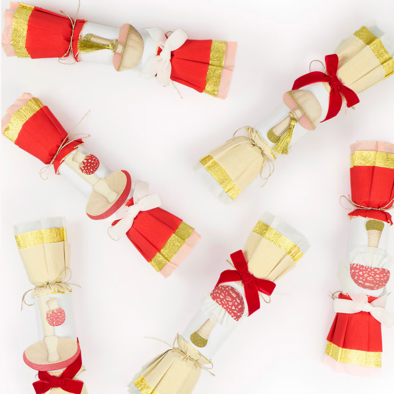 Five mushroom-shaped Christmas crackers arranged on a white background. Each cracker features a cream-colored body, a red pleated paper top, a red ribbon bow, and a gold glitter band.