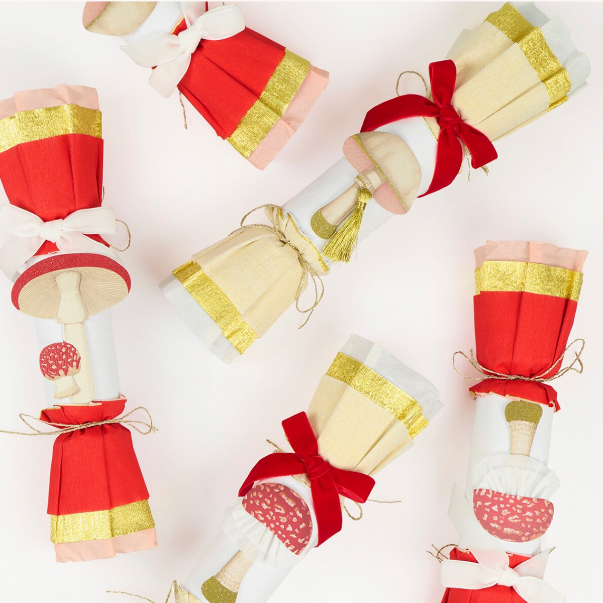 Five Christmas nutcracker-style crackers decorated with red and gold paper, white ribbons, and mushroom illustrations, arranged on a white background.