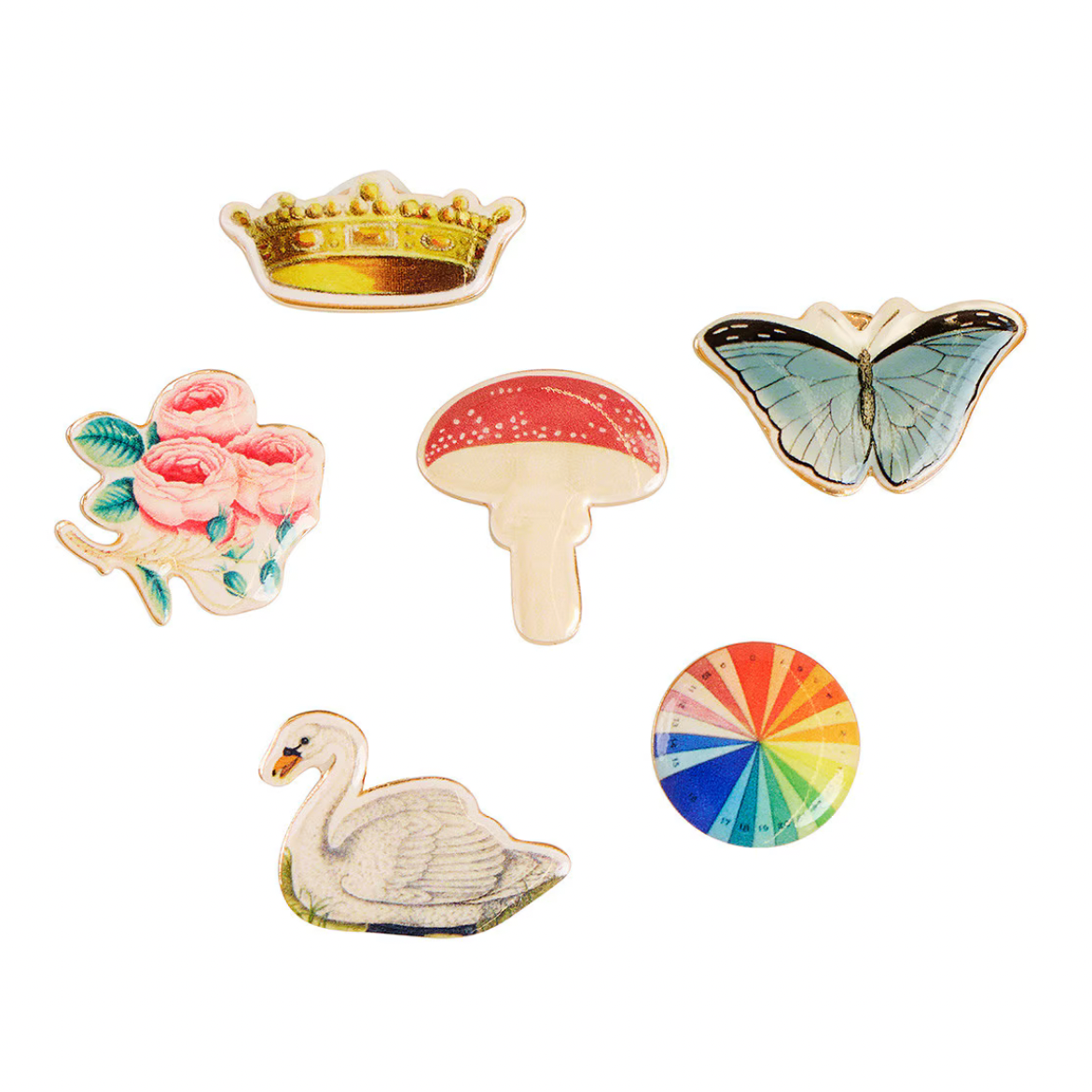 Six decorative enamel pin or brooch designs arranged on a plain white background: a gold crown, pink roses, a red-and-cream mushroom, a blue-and-green butterfly, a white swan, and a circular multicolor wheel.