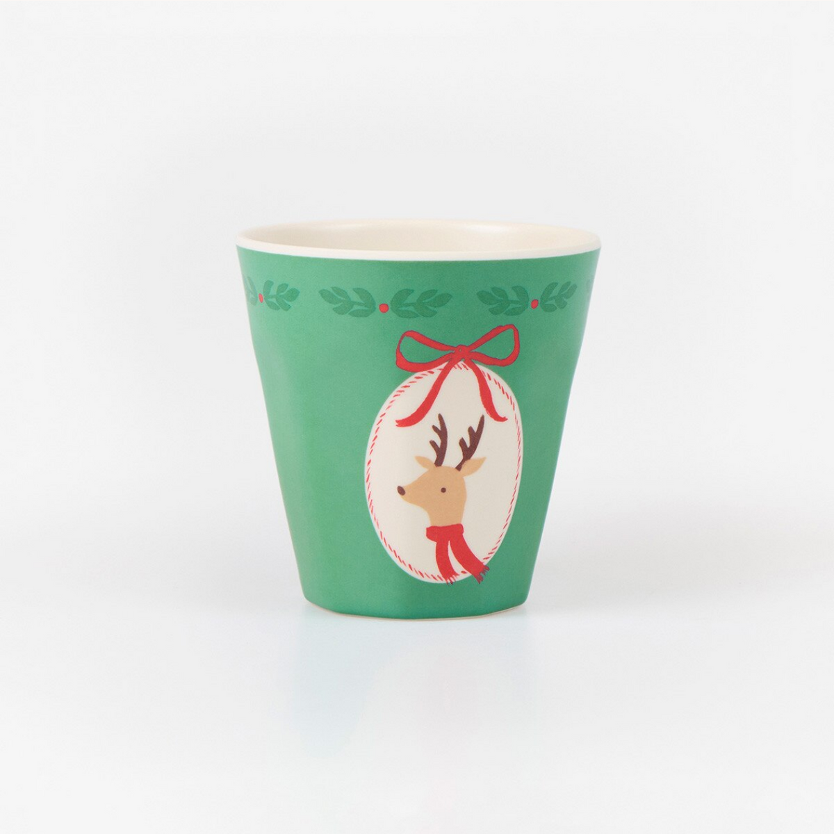 A green cup with a festive Christmas design, featuring a white oval with a reindeer wearing a red scarf and bow, and green holly leaves around the rim, on a white background.