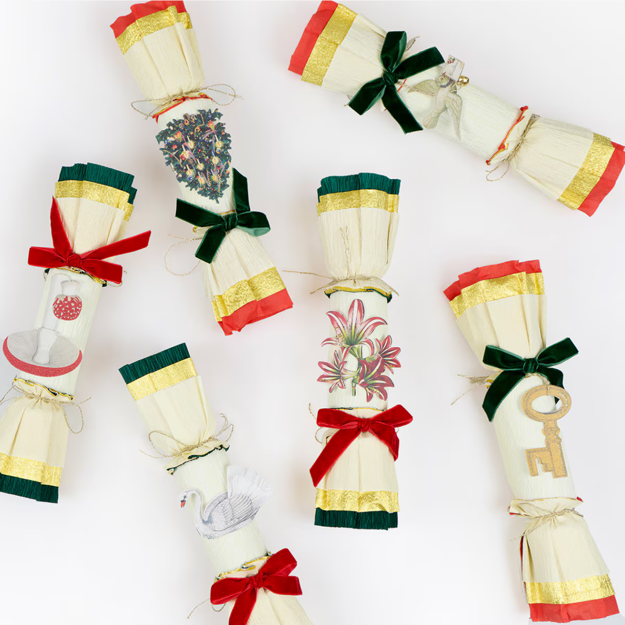 Six vintage-style Christmas cracker ornaments arranged on a plain white background. The crackers are off-white with colorful striped bands in red, green, and gold, tied with ribbon bows, and decorated with floral prints, a swan illustration, and a wooden key.