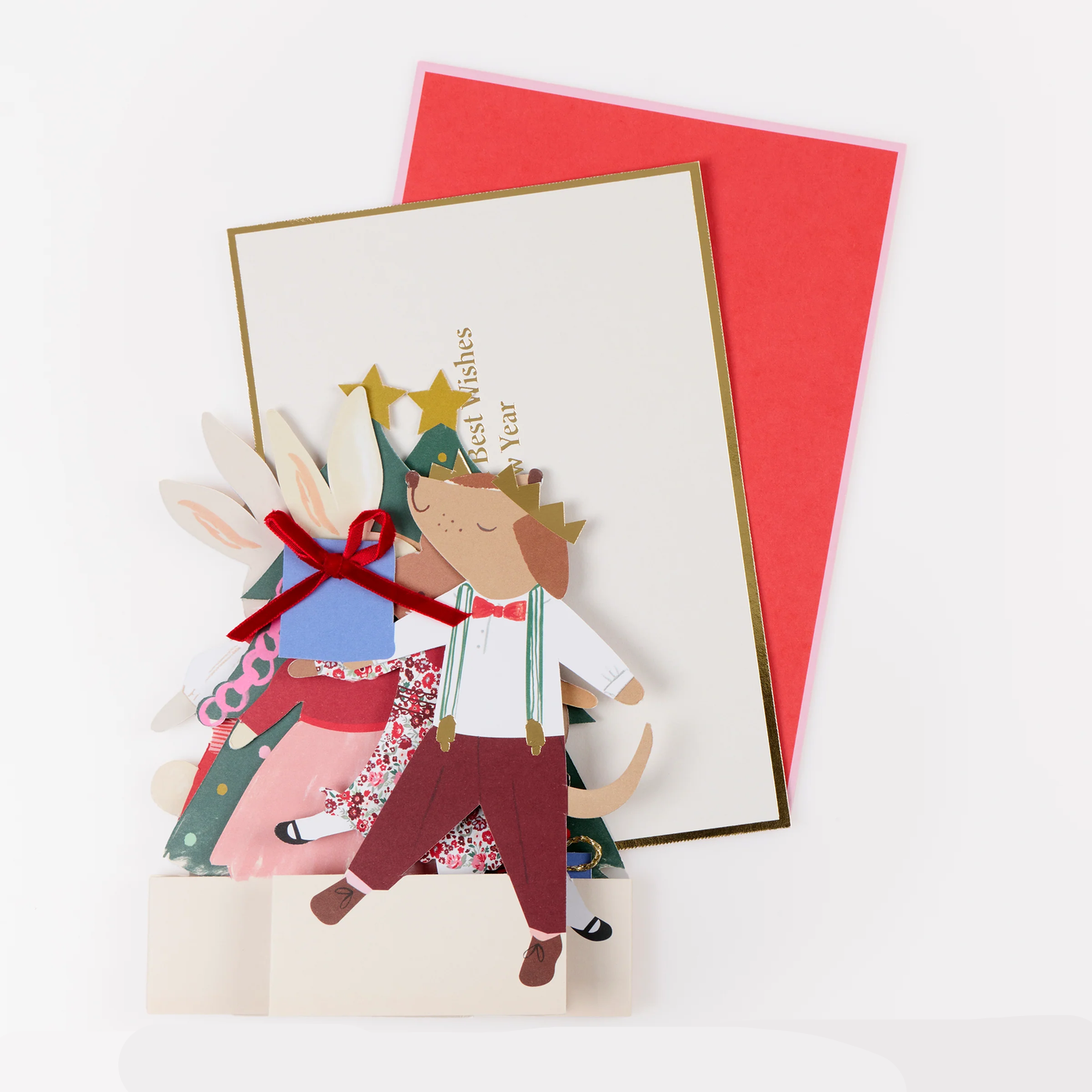 A handmade layered paper pop-up greeting card with a festive Christmas scene featuring a dog, rabbit, tree, and stars, shown with a red envelope on a white background.