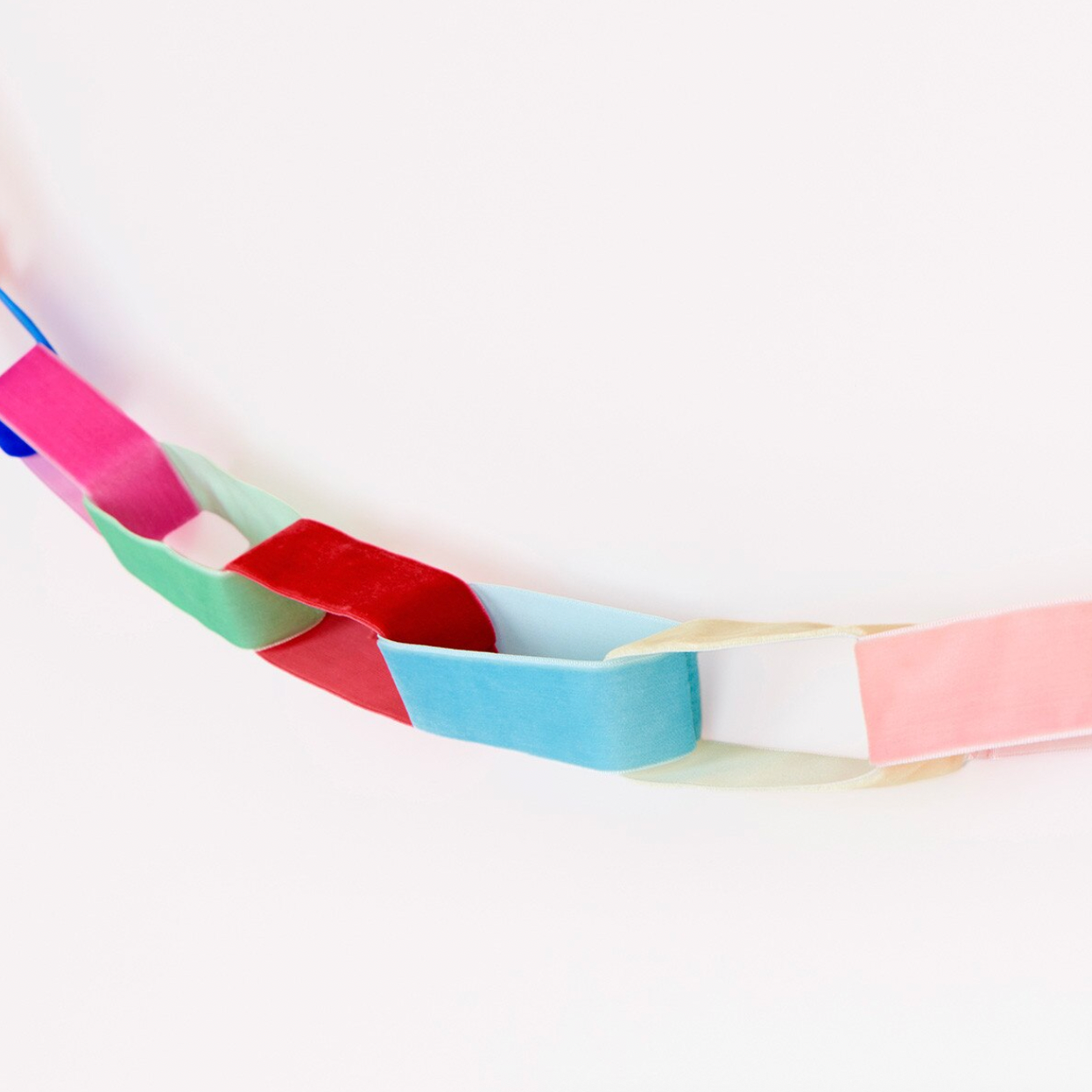 A handmade paper chain garland made of alternating colored paper links in blue, pink, red, green, and white, draped diagonally across a plain white background.