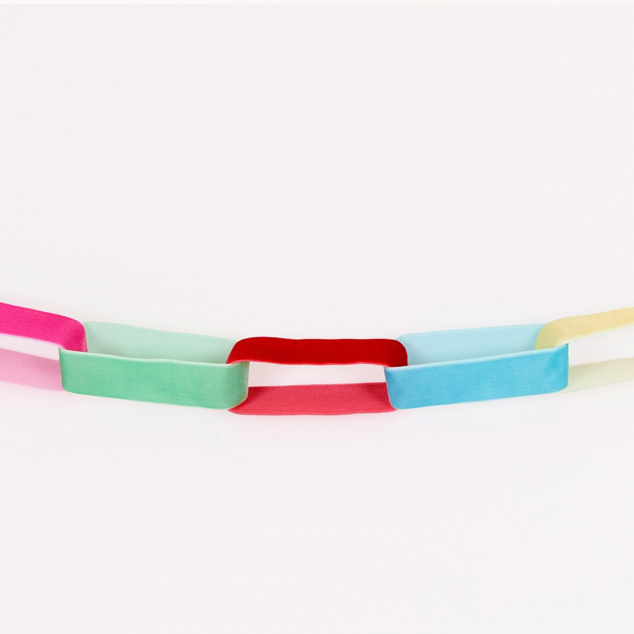 A pastel paper chain garland with alternating colored rectangular links, including pink, mint green, red, light blue, and pale yellow, arranged in a curved line against a plain white background.