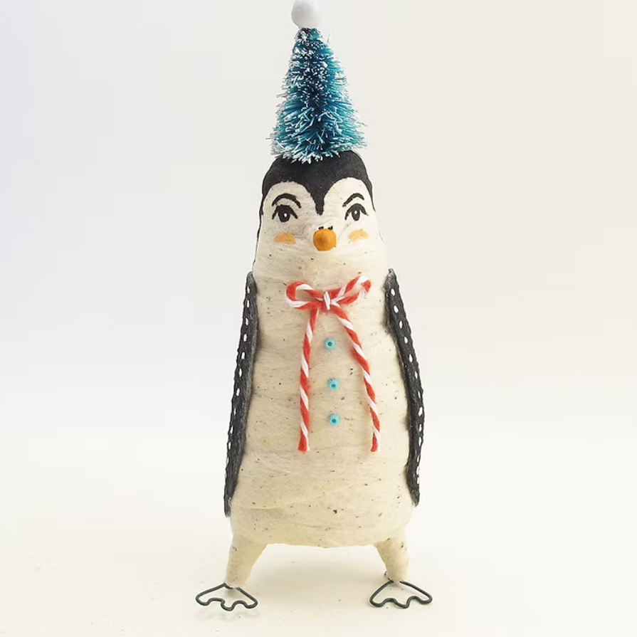 A handmade penguin figurine made from a textured ceramic or clay egg, decorated with a black and white patterned body, a red and white striped candy cane scarf, and a small blue tinsel Christmas tree hat, set against a plain white background.